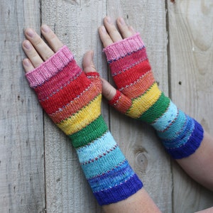 Könnte beinhalten: Ein Paar regenbogenfarbene Fingerlose Handschuhe mit einem Farbmuster in Pink, Rot, Orange, Gelb, Grün, Blau und Lila.