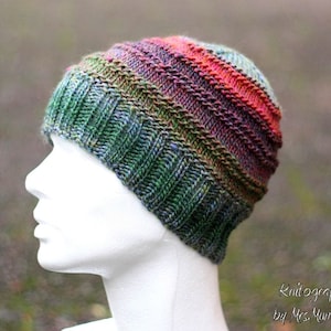Könnte beinhalten: Eine bunte gestreifte Strickmütze in Grün, Rot und Lila. Die Mütze ist aus weichem Garn gefertigt und hat eine lockere Passform.