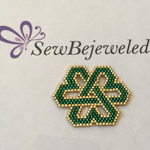 May include: A green and gold beaded knot design, resembling a four-leaf clover, with the text "SewBejeweled" above it.