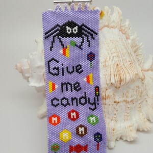 May include: Purple beaded bracelet featuring a spider, candy corn, and the text "Give me candy!"