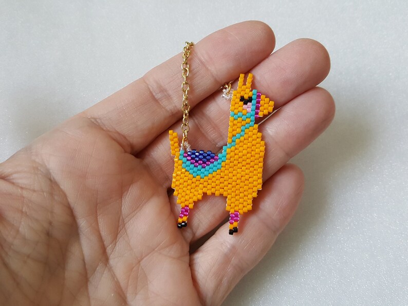 May include: A yellow beaded llama charm necklace with a gold chain. The llama has blue, pink, and purple details on its saddle.