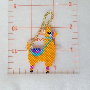 May include: A beaded llama keychain with a gold chain. The llama is orange with a turquoise, purple, and pink saddle. The keychain is approximately 2 inches tall.