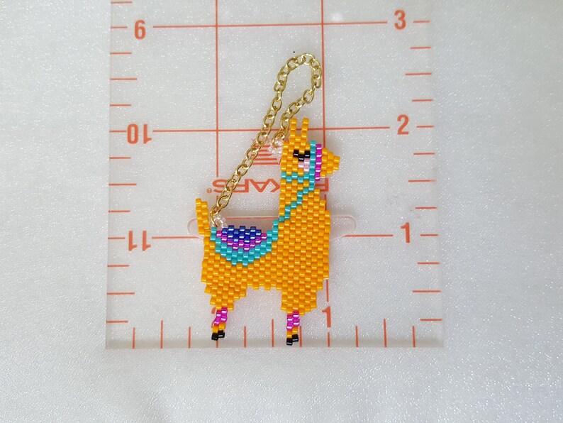 May include: A beaded llama keychain with a gold chain. The llama is orange with a turquoise, purple, and pink saddle. The keychain is approximately 2 inches tall.