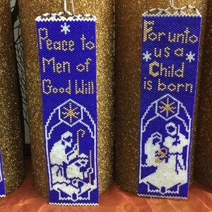 May include: Four blue and white beaded Christmas ornaments with gold lettering. The ornaments feature different Christmas scenes and verses. The ornaments read "Peace to Men of Good Will", "For unto us a Child is born", "And there appeared an Angel", and "Star of Wonder".