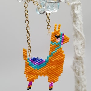 May include: A beaded llama charm with a gold chain. The llama is orange with blue, pink, and purple accents.