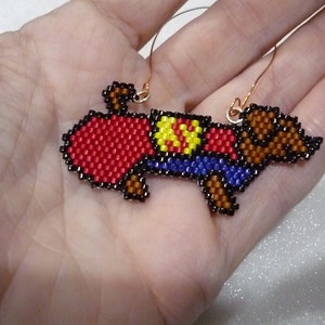May include: A beaded dachshund ornament with a red, yellow, and blue costume. The ornament is hanging from a gold wire.