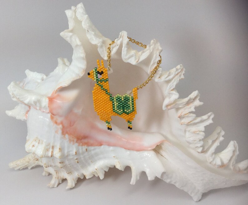 May include: A beaded llama charm with a gold chain, hanging from a white seashell.