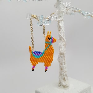 May include: A beaded llama ornament with a gold chain. The llama is orange with blue, purple, and pink details.
