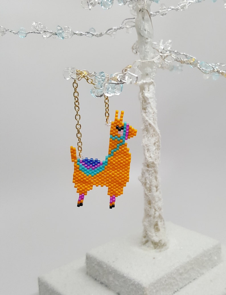 May include: A beaded llama ornament with a gold chain. The llama is orange with blue, purple, and pink details.
