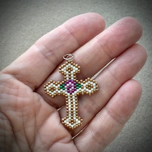 May include: A white and gold beaded cross with a pink and green flower in the center.