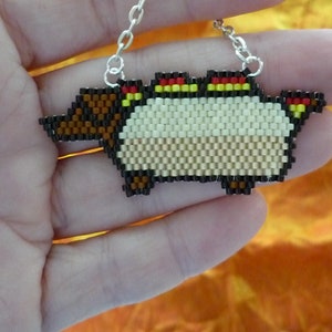 May include: A beaded necklace featuring a pixelated design of a brown and white creature with red and yellow accents. The creature has a long snout and a rounded body.