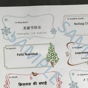 May include: A printable sheet with Christmas greetings in different languages. The sheet features a festive design with snowflakes and a Christmas tree. The greetings include "Merry Christmas" in English, "Feliz Navidad" in Spanish, "Frohe Weihnachten" in German, and more.