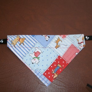 May include: A blue and red dog bandana with a patchwork design featuring various dog illustrations. The bandana is attached to a black strap with paw prints.