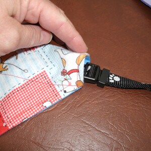 May include: A close-up of a fabric dog lead with a black plastic buckle and a paw print design. The lead is made of a patchwork fabric with a blue, white and red checked pattern.