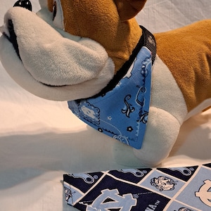May include: Two dog bandanas, one blue with a paisley pattern and the other blue and white with a repeated pattern of the University of North Carolina Tar Heels logo and the word "Carolina".