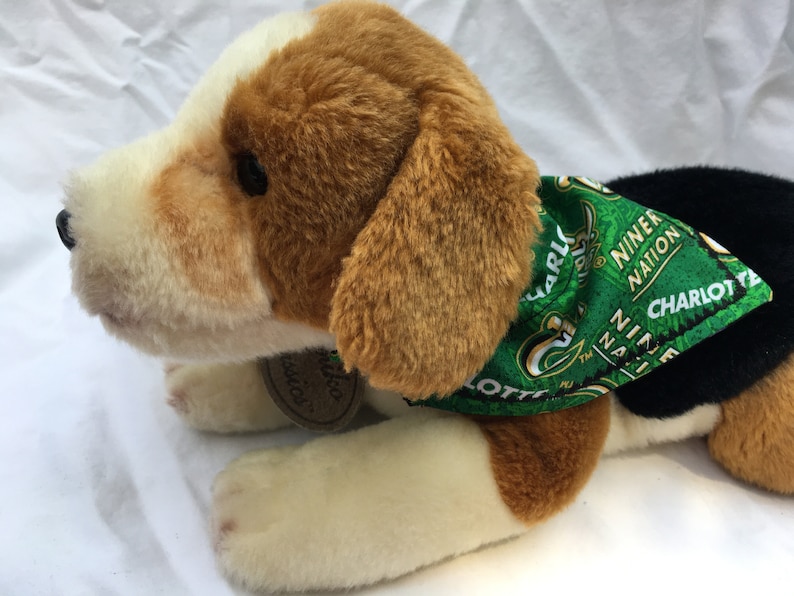 May include: A brown and white plush dog wearing a green bandana with the text "Charlotte 49er Nation" printed on it.