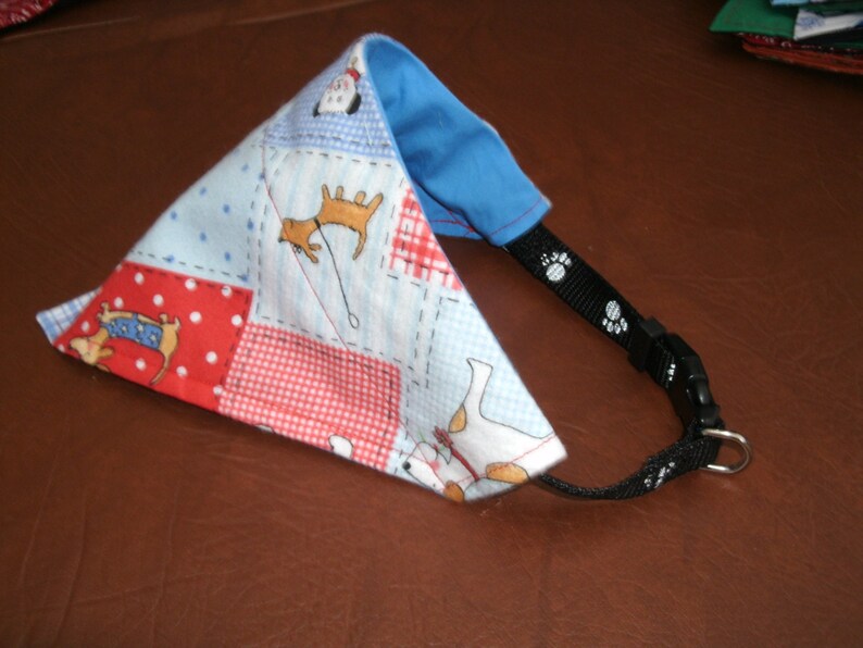 May include: A blue, red and white patterned dog bandana with a black adjustable strap and a silver buckle. The bandana features a variety of dog illustrations.