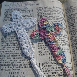 May include: A close-up of a crocheted bookmark with a floral design in shades of pink, blue, and white. The bookmark is placed on an open book of Psalms, with the text "Remember, O Lord, thy loving kindness and thy tender mercies, for they have been of old." visible.