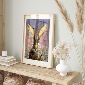 May include: A framed watercolor painting of a brown rabbit with large ears, set against a purple and pink background. The rabbit is looking directly at the viewer with a curious expression.