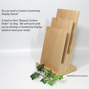 May include: A wooden countertop display stand with three shelves. The stand is made of light wood and has a natural finish. The stand is ideal for displaying items such as books, photos, or other small items. The stand is also available in custom sizes.