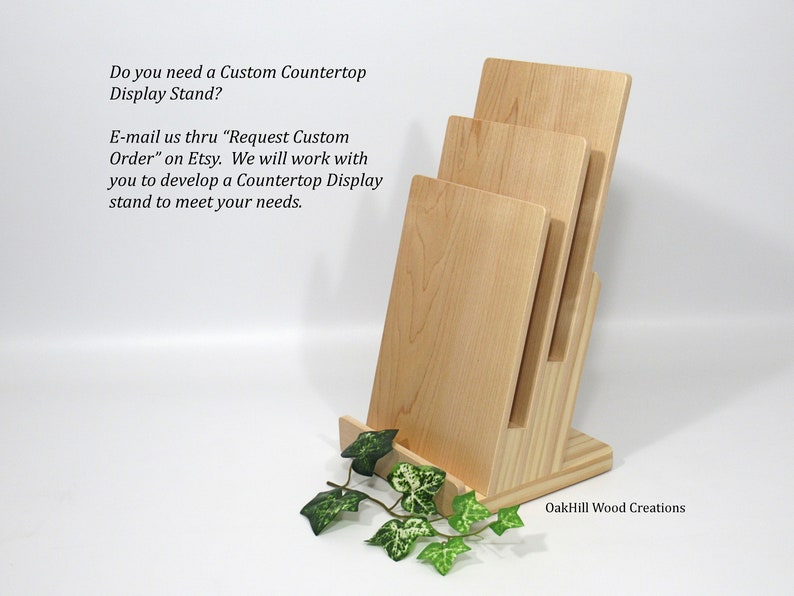May include: A wooden countertop display stand with three shelves. The stand is made of light wood and has a natural finish. The stand is ideal for displaying items such as books, photos, or other small items. The stand is also available in custom sizes.