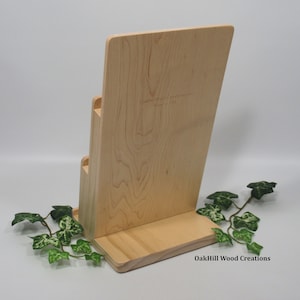 May include: A wooden magazine rack with three tiers. The rack is made of light wood and has a natural finish. The rack is labeled "OakHill Wood Creations".