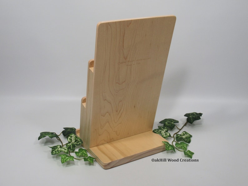 May include: A wooden magazine rack with three tiers. The rack is made of light wood and has a natural finish. The rack is labeled "OakHill Wood Creations".