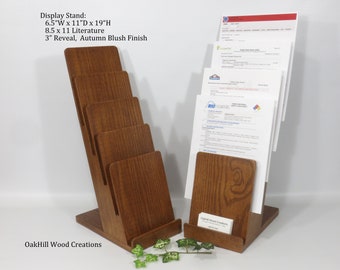 May include: A wooden magazine rack with five slots for holding literature. The rack is 6.5 inches wide, 11 inches deep, and 19 inches high. It has a 3-inch reveal and an autumn blush finish. The rack is made by OakHill Wood Creations.