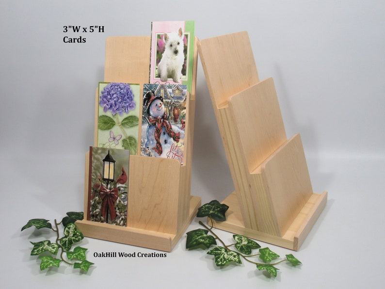 May include: Two wooden card holders, one with three slots and the other with four slots. The holders are made of natural wood and are designed to hold standard-sized greeting cards. The text "3"W x 5"H Cards" is visible on the left holder.
