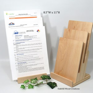 May include: A wooden magazine rack with three slots for holding papers. The rack is made of natural wood and has a light brown finish. The rack is 8.5 inches wide and 11 inches high. The rack is sitting on a white surface. OakHill Wood Creations is printed on the base of the rack.