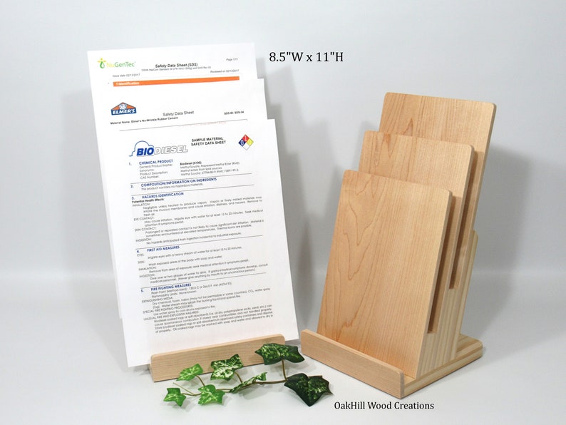 May include: A wooden magazine rack with three slots for holding papers. The rack is made of natural wood and has a light brown finish. The rack is 8.5 inches wide and 11 inches high. The rack is sitting on a white surface. OakHill Wood Creations is printed on the base of the rack.