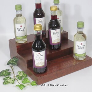 May include: A three-tiered wooden wine rack with a dark brown stain. The rack is filled with five miniature bottles of wine, including Sutter Home Sauvignon Blanc and Gallo Family Pinot Noir.