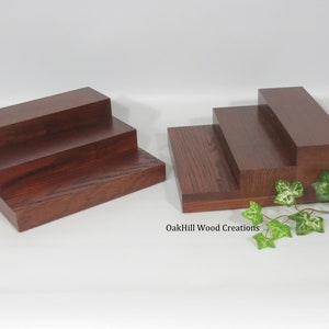 May include: Two wooden three-tiered risers, made of dark stained wood, with a leafy green plant in the foreground. The text "OakHill Wood Creations" is visible in the bottom right corner of the image.