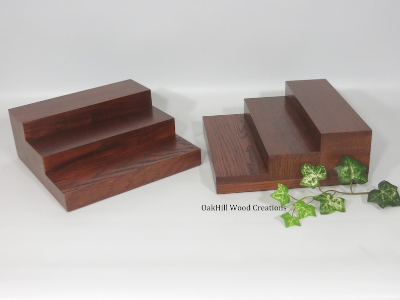 May include: Two wooden three-tiered risers, made of dark stained wood, with a leafy green plant in the foreground. The text "OakHill Wood Creations" is visible in the bottom right corner of the image.