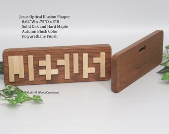 May include: A wooden plaque featuring an optical illusion of the word "Jesus" in a light wood colour against a dark wood background. The plaque measures 8.62 inches wide, 0.75 inches deep, and 3 inches high. It is crafted from solid oak and hard maple with an autumn blush colour and a polyurethane finish. The plaque is labelled "OakHill Wood Creations".