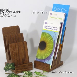 May include: Two wooden brochure holders, one with three slots and the other with one slot. The brochure holder with three slots is 3.5 inches wide by 5.75 inches deep by 8.37 inches high. The brochure holder with one slot is 3.5 inches wide by 8.5 inches high. Both holders are made of dark walnut wood and have a 1.5 inch reveal. The brochure holder with one slot has brochures inserted that say "Dry Eye", "Floaters and Flashes", and "Age-Related Macular Degeneration (AMD)".