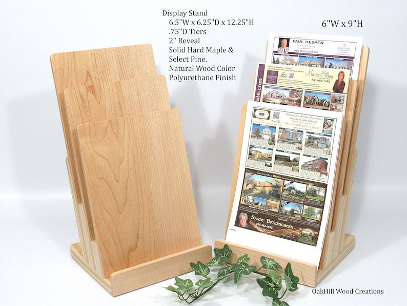 May include: A wooden display stand with three tiers for holding brochures or leaflets. The stand is made of solid hard maple and select pine, with a natural wood colour and polyurethane finish. It measures 6.5 inches wide by 6.25 inches deep by 12.25 inches high. Each tier is 0.75 inches deep and has a 2-inch reveal. The stand is shown with brochures featuring property listings.