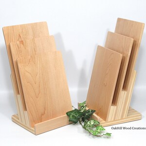 May include: Two wooden cutting board holders with four cutting boards stacked on each. The holders are made of light wood and have a natural finish. The cutting boards are also made of light wood and have a natural finish. The holders are sitting on a white surface. OakHill Wood Creations is printed on the bottom right corner of the image.