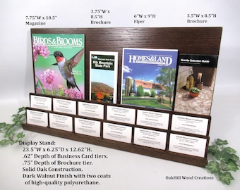 May include: A dark walnut display stand with multiple brochure and business card slots. The stand holds magazines, brochures, and flyers, including one with a hummingbird and the text "BIRDS & BLOOMS". The stand is 23.5"W x 12.62"H.