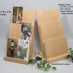 May include: Two wooden card display stands with three slots each. The stands are made of natural wood with a polyurethane finish. The stands are 6.75 inches wide, 5.75 inches deep, and 12.12 inches high. The slots are 4.25 inches high. The stands are designed to hold 3" x 5" cards.