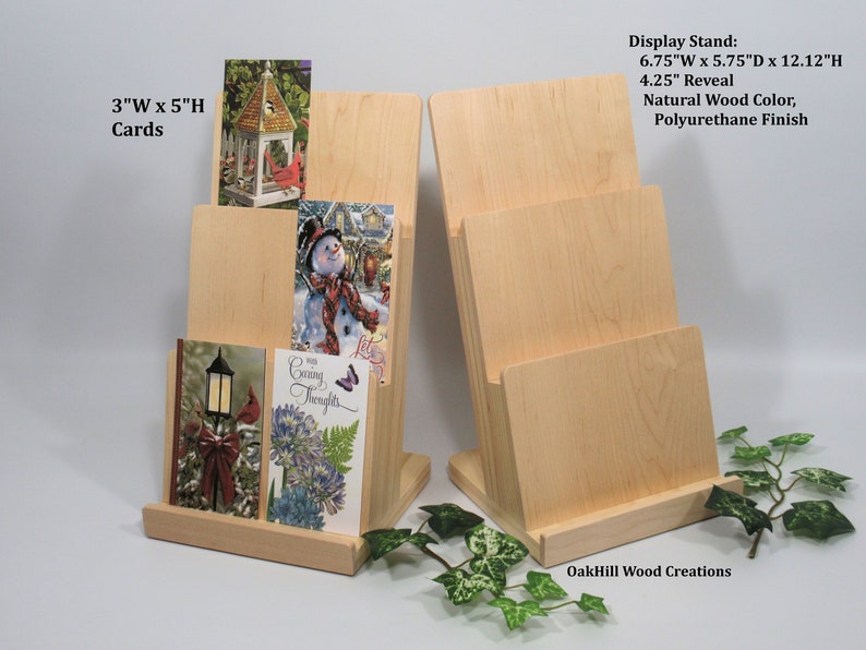 May include: Two wooden card display stands with three slots each. The stands are made of natural wood with a polyurethane finish. The stands are 6.75 inches wide, 5.75 inches deep, and 12.12 inches high. The slots are 4.25 inches high. The stands are designed to hold 3" x 5" cards.
