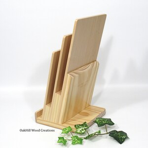 May include: Wooden magazine rack with three slots for holding magazines or papers. The rack is made of natural wood and has a simple, modern design. OakHill Wood Creations is printed on the base.