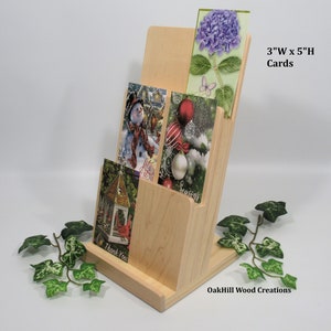 May include: A wooden card holder with three slots for displaying cards. The holder is made of natural wood and has a simple, elegant design. The cards are 3 inches wide by 5 inches high. The holder is labeled "OakHill Wood Creations".