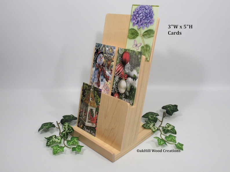 May include: A wooden card holder with three slots for displaying cards. The holder is made of natural wood and has a simple, elegant design. The cards are 3 inches wide by 5 inches high. The holder is labeled "OakHill Wood Creations".
