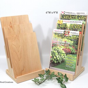 May include: A wooden magazine rack with four slots to hold magazines. The rack is made of natural wood and is 15.2 cm wide by 22.9 cm high. The rack is holding three copies of "Garden Gate" magazine.
