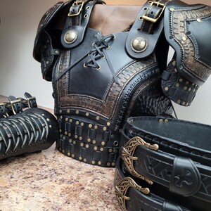 May include: Black leather armor set with intricate embossed designs and brass-colored rivets and buckles. The set includes a chest piece, shoulder guards, arm guards, and a belt, all with a medieval or fantasy theme.