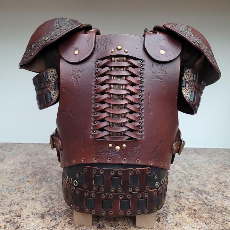 May include: A handcrafted, brown leather breastplate with intricate detailing. The armor features shoulder pauldrons, woven back panel, and decorative metal rivets. The design suggests a medieval or fantasy theme.