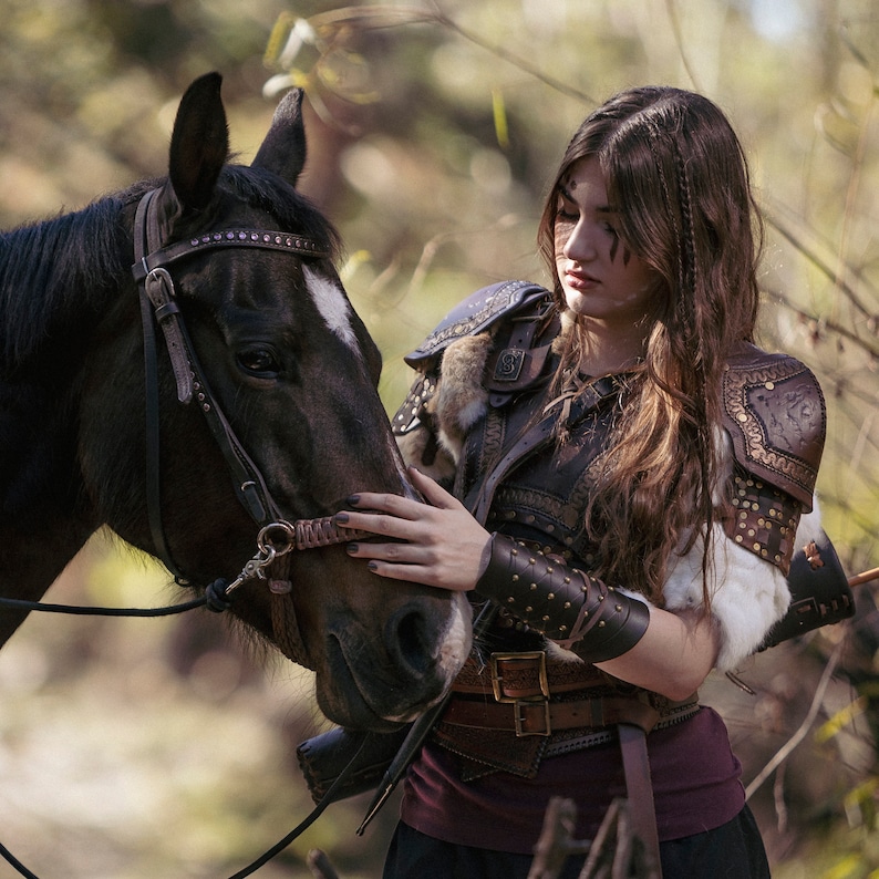 May include: A dark brown horse with a white blaze on its face is being petted by a person wearing brown leather armor with fur accents. The armor includes shoulder pads and arm guards. The person is wearing a burgundy top and black skirt.