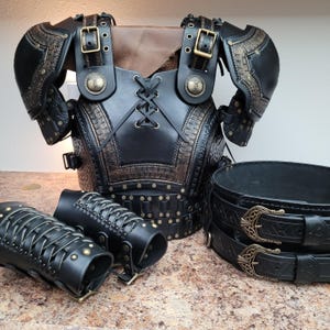 May include: Black leather armor set with intricate embossed designs and brass-colored accents. The set includes a chest piece, shoulder guards, arm bracers, and a belt with decorative buckles. The armor is designed with buckles and lacing for adjustment.