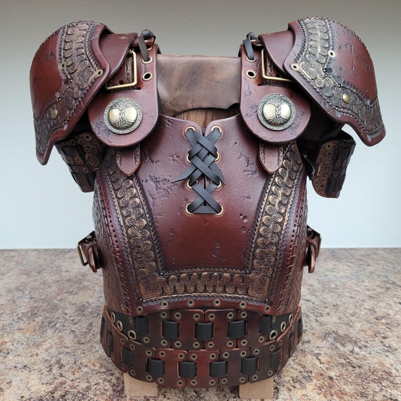 May include: A handcrafted brown leather breastplate with shoulder guards. The armor features intricate embossed designs, brass accents, and a laced closure. Decorative metal medallions with a tree design are on the shoulder guards. The armor is designed to be worn.